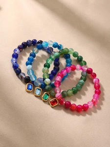Macro shot of colorful agate bead bracelets with gold-framed emerald cut stone pendants