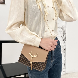 Brown crossbody chain bag with vintage pattern and gold deer tassel closure worn by a model