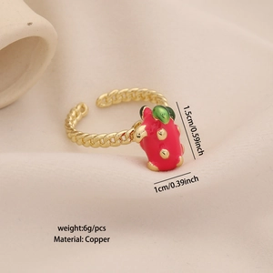 Close-up of golden copper ring with red pitaya enamel charm on beige fabric background