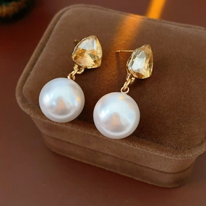 Detailed view of triangle pearl stud earrings with gold accents on brown velvet