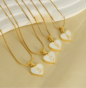 Macro view of four gold-plated heart-shaped pendants with shell inlay and letter engraving