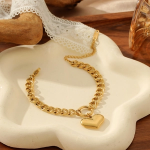 Golden double chain bracelet with heart pendant and toggle clasp on a decorative tray