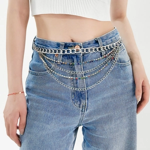 Détail d'une chaîne de taille argentée multicouche avec strass colorés sur un jean