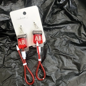 Macro detail of creative blood bag earrings with red liquid and AB blood type label