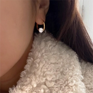 Detail view of a gold cubic zirconia hoop earring worn with a white cozy coat
