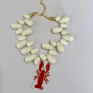 Close-up of white beaded ocean necklace featuring a detailed red lobster pendant and gold clasp