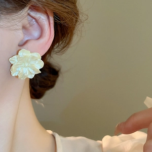 Close-up of cream camellia flower earring with pearl luster finish on a female model