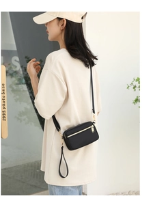 Model wearing a black nylon crossbody bag with multi-zipper layers and gold hardware