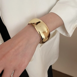 Dettaglio di un ampio bracciale dorato irregolare con superficie lucida sul polso