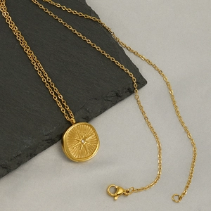 Gold stainless steel starburst coin necklace with zircon on a slate and fabric background