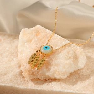 Gold evil eye necklace with leaf pendants on stone and white silk background