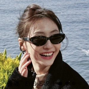 Detail of black cat-eye sunglasses with silver metal hinges worn by a woman outdoors