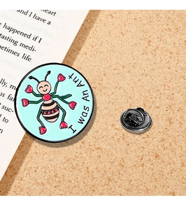 Close-up of circular enamel ant brooch with I was An Ant text and metal pin back