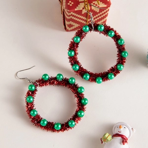 Close-up of red tinsel Christmas wreath earrings with green beads and silver hooks