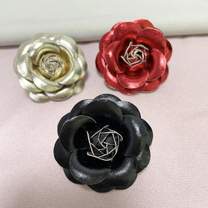 Detailed macro view of leather camellia brooches in gold, red, and black on fabric