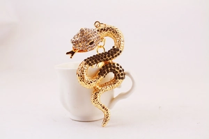 Close-up of golden snake keychain with rhinestones in a white mini ceramic cup