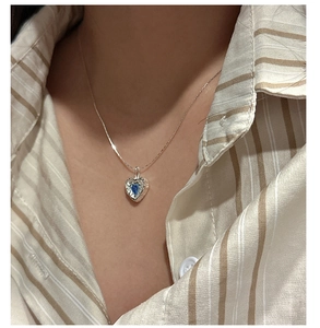Detail of S925 silver necklace with textured heart pendant and blue zircon on a model