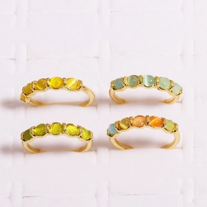 Detail of four gold rings with colorful round cat-eye stones on a white grid tray