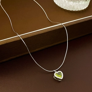 Detailed view of a green heart-shaped zircon pendant on a silver-toned cable chain necklace