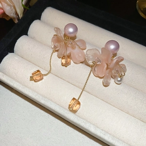Dettaglio di orecchini a petalo rosa con perle e nappe in una scatola per gioielli