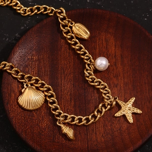 Detail of 18K gold-plated ocean-themed bracelet with seashells and pearl on wood