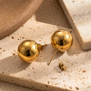 Polished gold sphere stud earrings in stainless steel on a minimalist stone background
