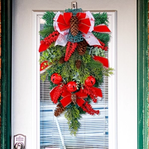 Christmas door wreath with red velvet bow pine cones and bells on white wooden door
