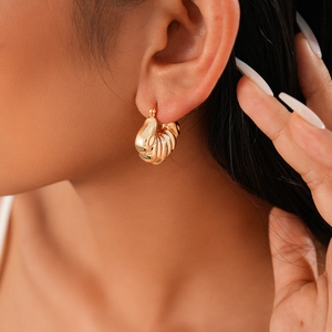Close-up of golden geometric twisted shell earrings worn by a model for a stylish look