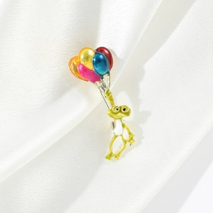Détail d'une broche grenouille avec ballons en émail colorés sur fond de satin blanc
