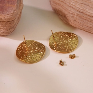 Macro detail of gold square stud earrings with irregular hammered texture on stone base