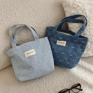 Detail of denim tote bag showing delicate white bow embroidery and canvas brand label