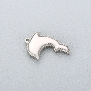 Macro detail of a silver dolphin pendant with white enamel inlay and beaded metal edges