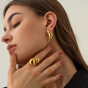 Close-up of golden croissant earrings and pebble ring worn by model on beige background