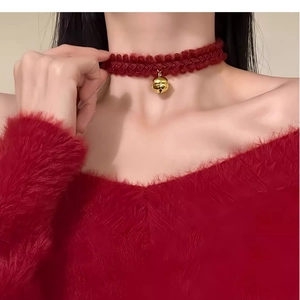 Close-up of a dark red lace choker with a polished gold bell pendant on a model