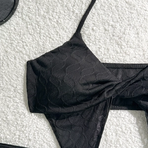 Detail eines schwarzen Bikini-Oberteils mit gewellter Textur und feinen Schultergurten