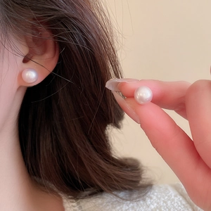 Close-up of elegant 8-10mm round pearl earrings with subtle pink luster on earlobe