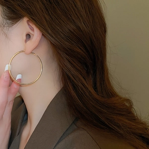 Side view detail of a large polished gold round hoop earring worn by a female model