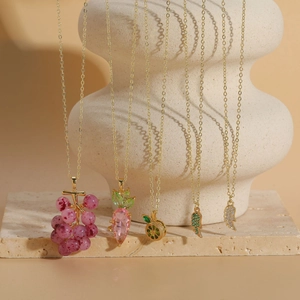 Close-up of gold necklaces with fruit pendants and crystals on textured stone base