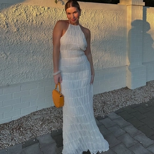 Detail of white backless maxi dress featuring textured pleated fabric and halter neck style