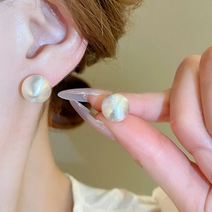 Detail of matte cream round stud earrings featuring a brushed finish and pearl luster