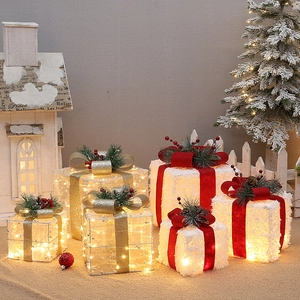 Close-up of lighted white flocking and mesh Christmas gift boxes with festive pine accents