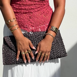 Eleganter goldener hohler Armreif und stapelbare Ringe mit schwarzer gewebter Clutch