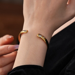 Close-up of a gold open bangle with sparkling rectangular and round zircon stones on wrist
