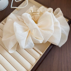 Detailed close-up of cream chiffon bow hair claw clip on jewelry display tray