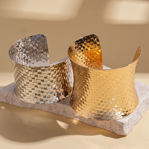 Wide woven metal cuff bracelets in gold and silver finish on natural stone background