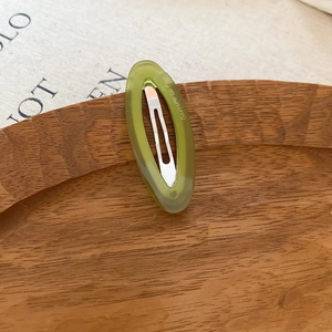 Detail view of oval grass green acetate hair clip with gold lettering on a wooden tray