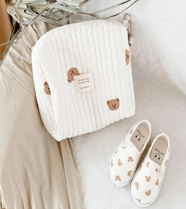 Flat lay of cream quilted pouch and shoes featuring brown bear embroidery details