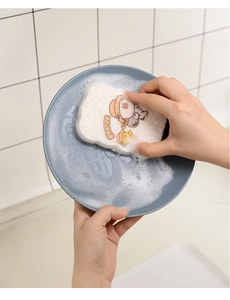 Kitchen wood pulp sponge creating rich white foam while cleaning a gray ceramic plate