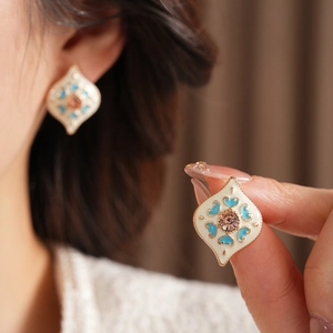 Detailed close-up of diamond-shaped gold earrings with white enamel and pink heart crystal