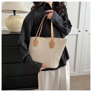 Detailed close-up of large straw tote bag with brown leather handles on a model shoulder